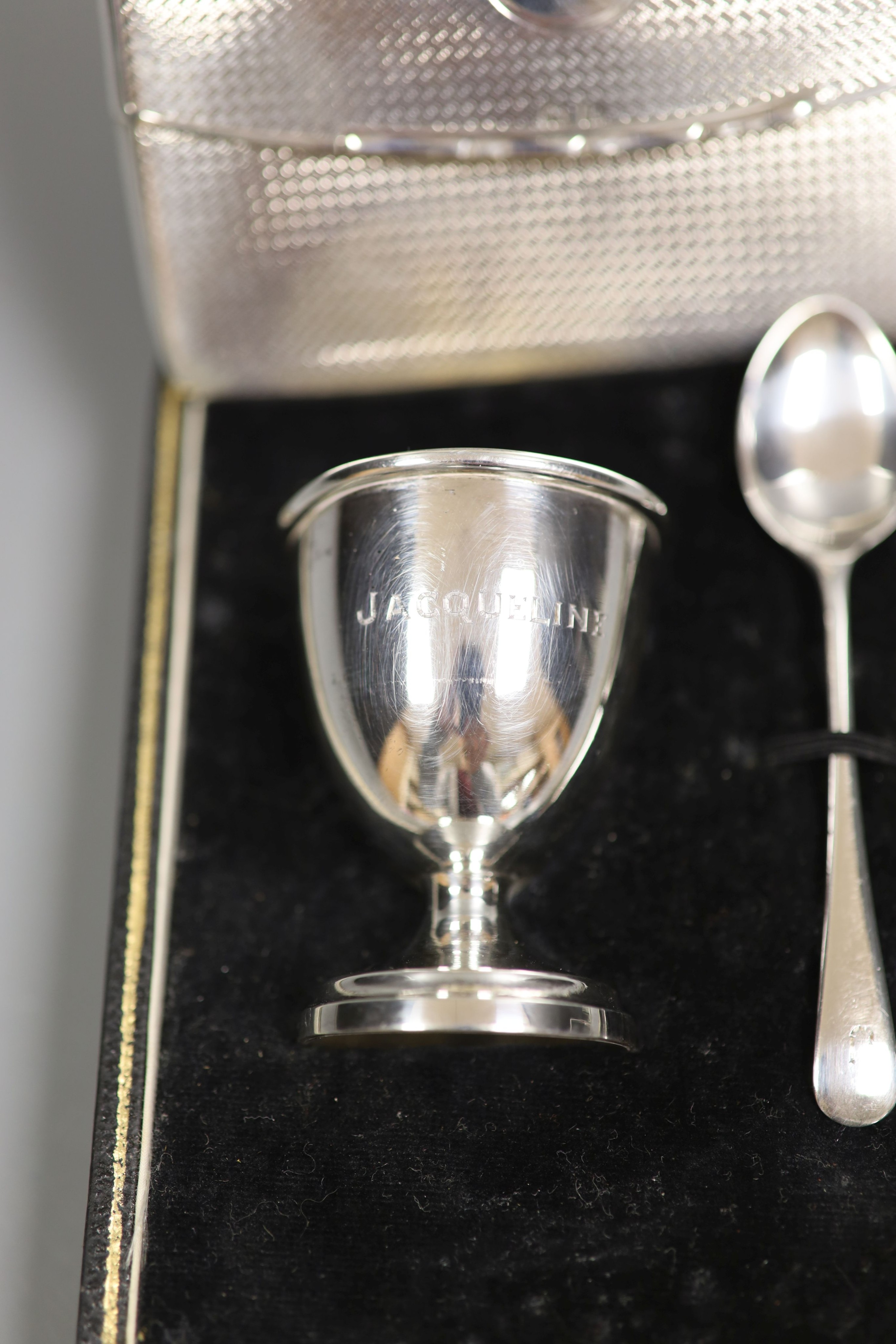 An Edwardian engine tuned silver 'envelope' card case, Birmingham, 1909, 10.4cm and a cased silver christening egg cup and spoon.